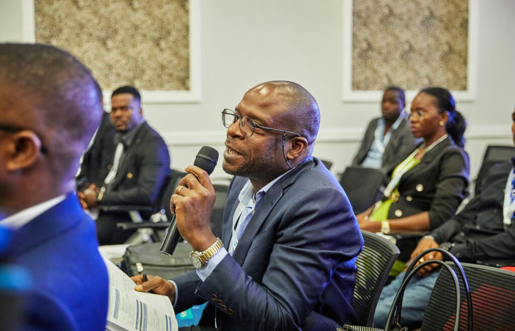 A participant in a suit asks a question during a professional conference, holding a microphone.