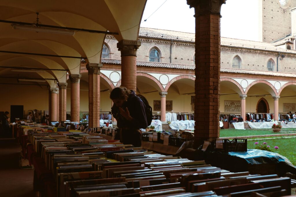A person explores a book market in a historic courtyard with arched columns and a vibrant atmosphere.