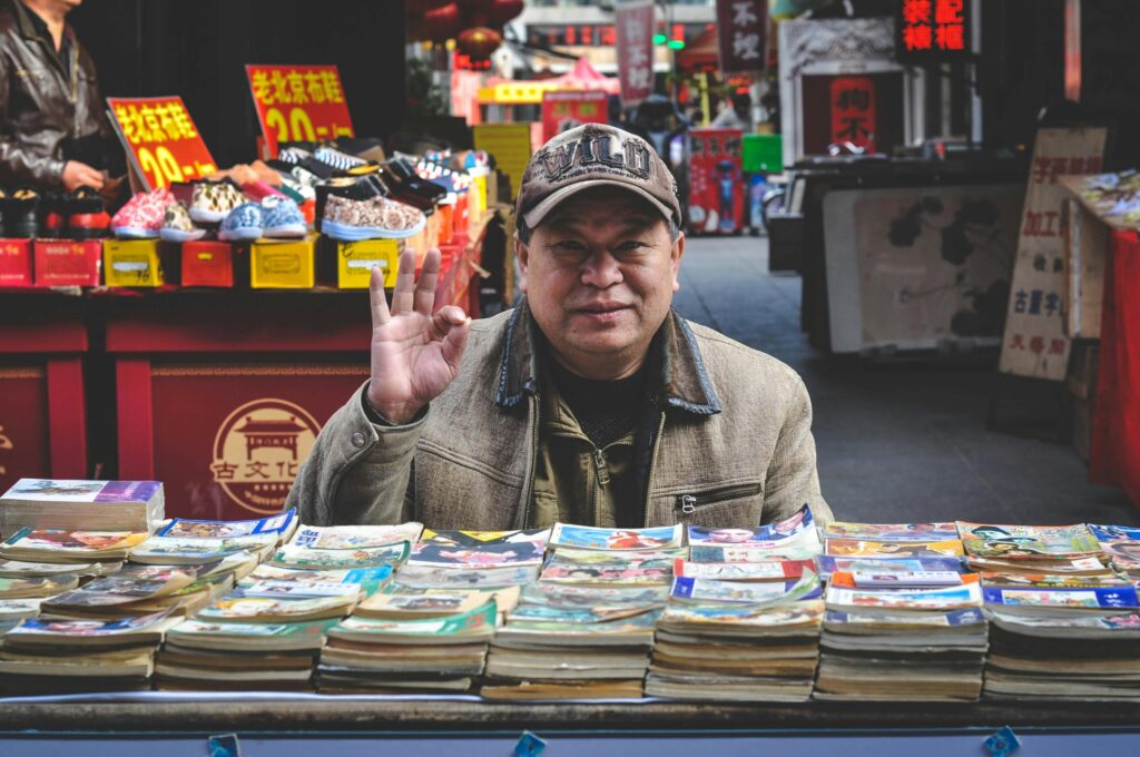 An elderly vendor selling books at a vibrant Tianjin street market.